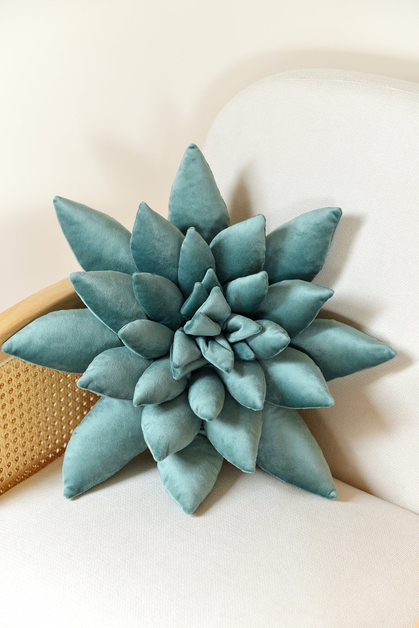 Large succulent shaped velvet decor pillow in teal colour placed on an ivory rattan armchair.