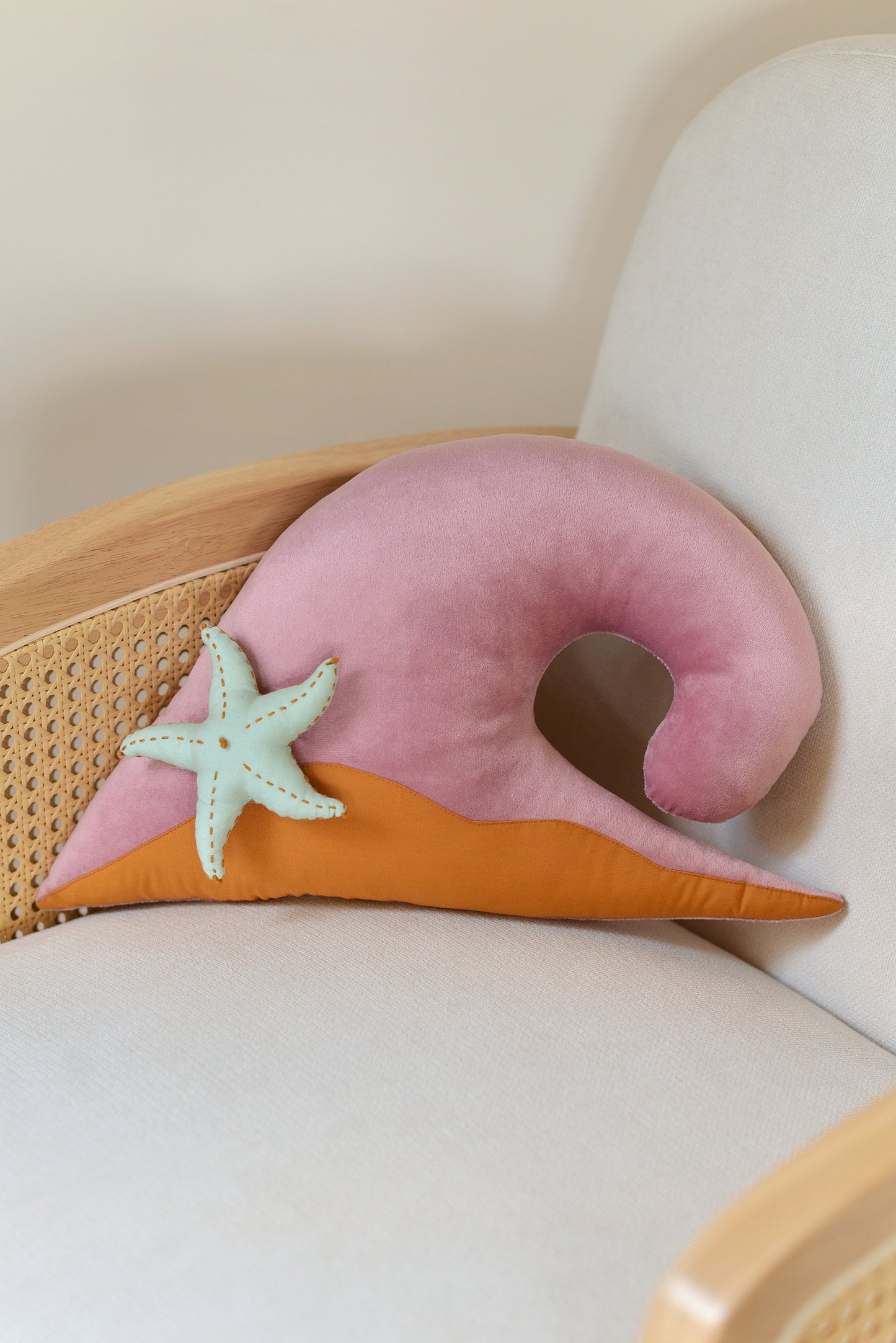 Lilac wave shaped decor pillow with ochre sandy base and mint green starfish on an ivory rattan armchair.