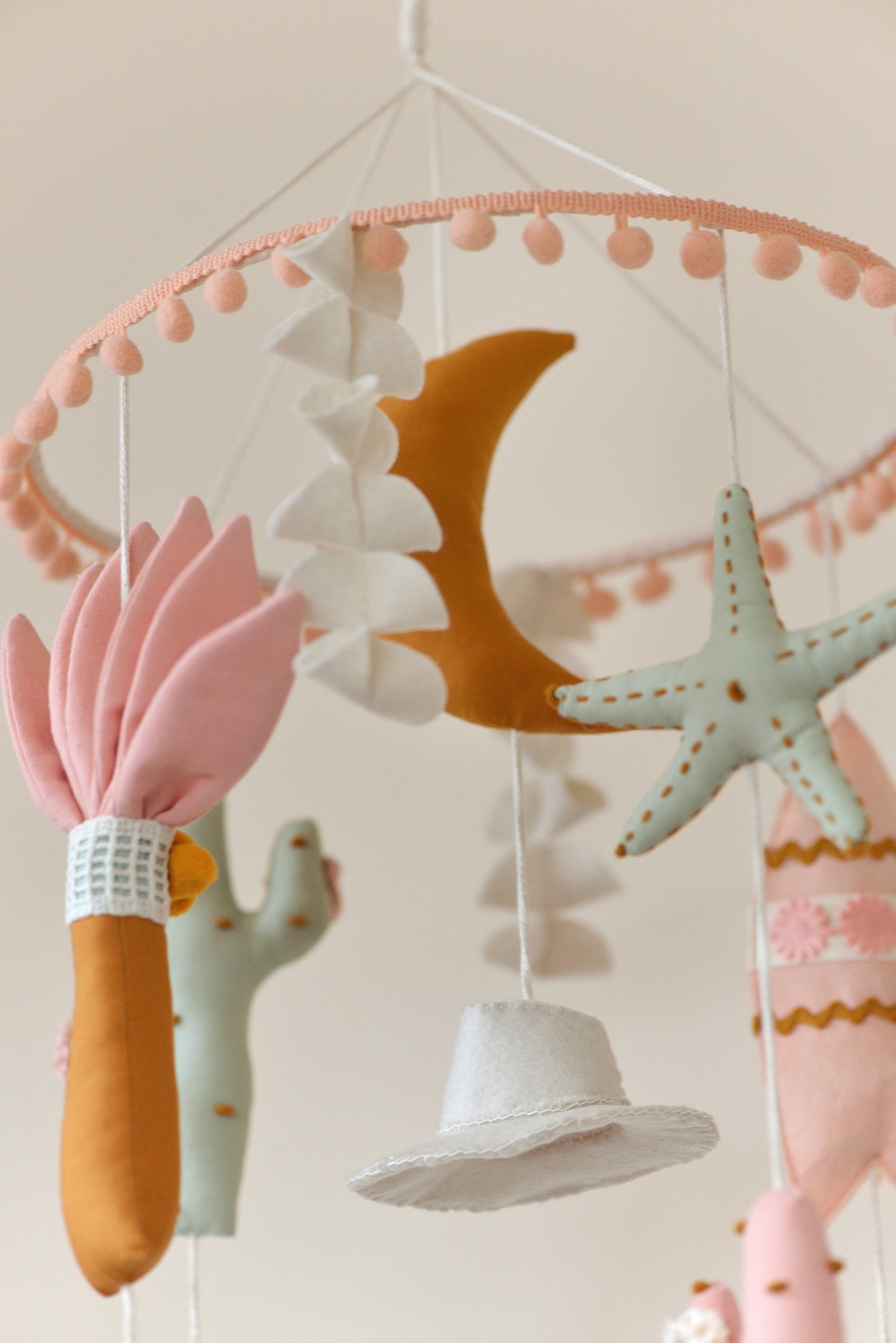 Baby nursery mobile with colorful hanging figures against a light background: moon, palm, starfish, cowboy hat, surf board.