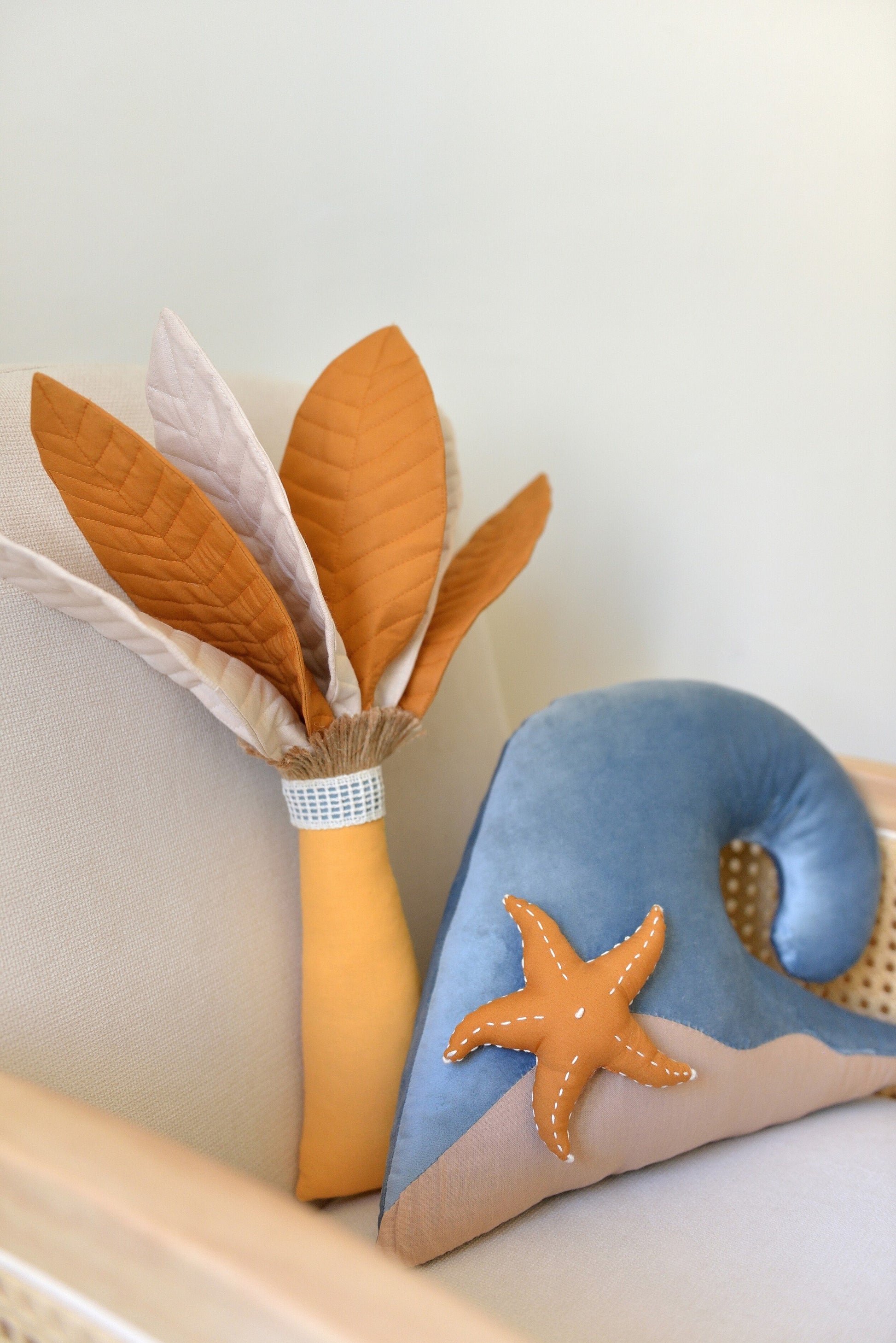 Handmade palm tree and ocean wave shaped decor pillow with a starfish placed on a rattan armchair against a white wall.