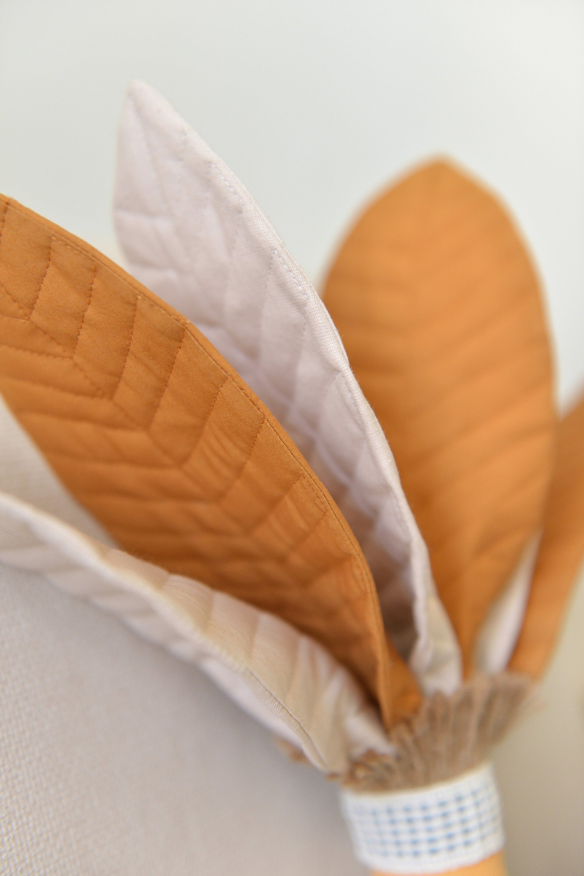 Close-up of the ivory and ochre mixed fronds of a handmade palm tree decor pillow against a light wall.