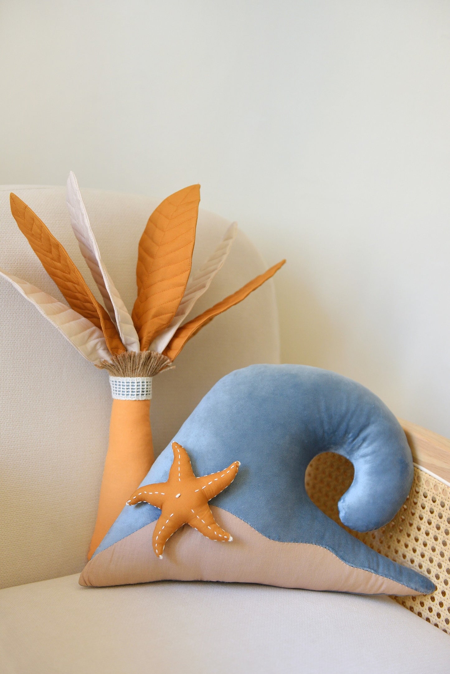 Handmade palm tree and ocean wave shaped decor pillow with a starfish placed on a rattan armchair against a white wall.