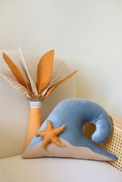 Handmade palm tree and ocean wave shaped decor pillow with a starfish placed on a rattan armchair against a white wall.