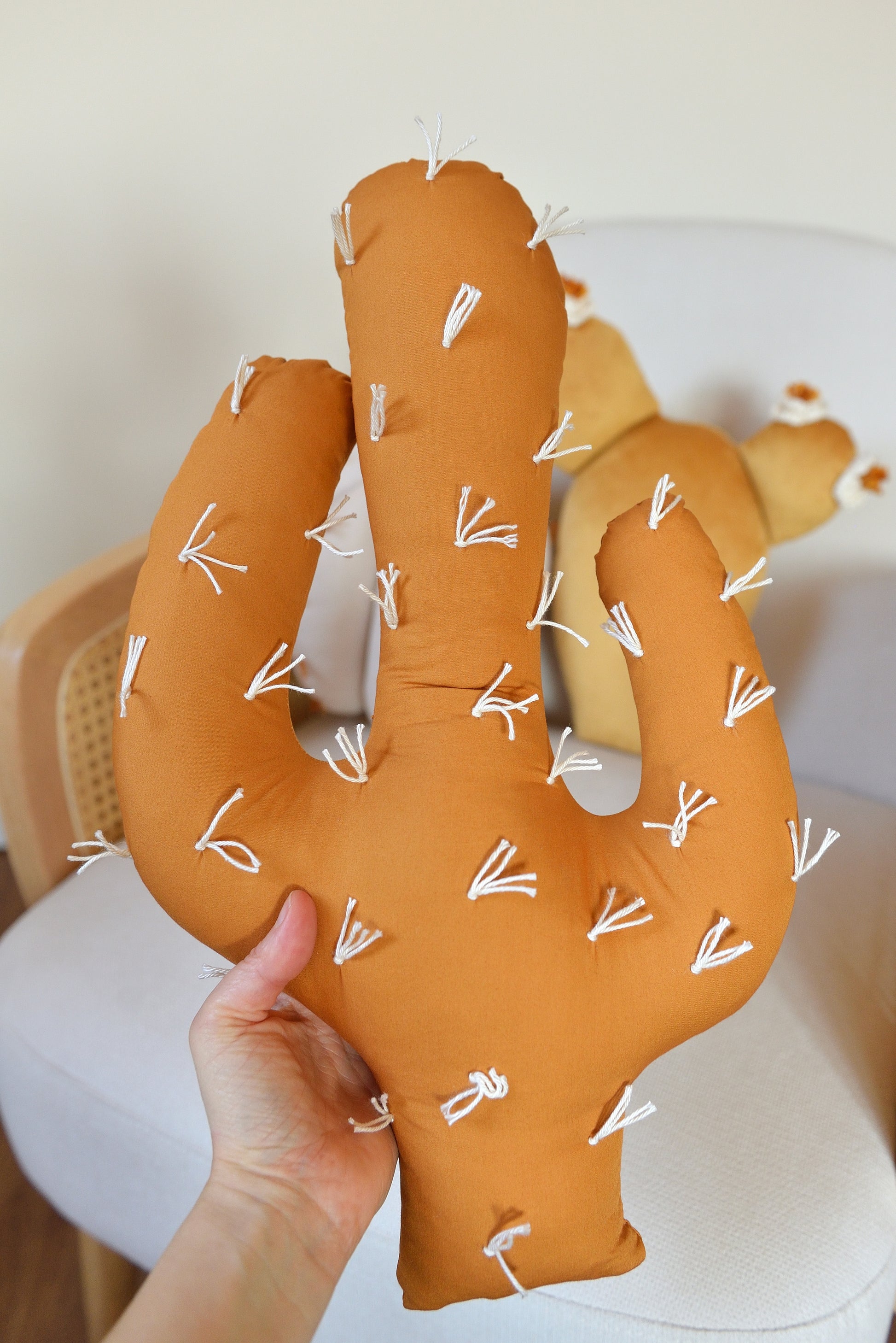 Hand holding ochre saguaro cactus shaped decor pillow.