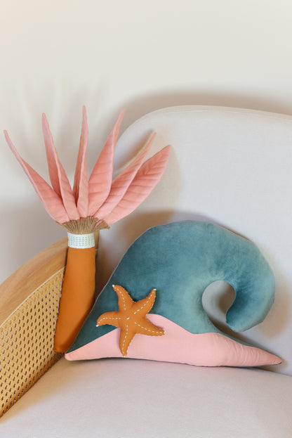 Palm tree and ocean wave shaped decor pillow placed on an ivory armchair.