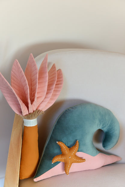 Palm tree and ocean wave shaped decor pillow placed on an ivory armchair.