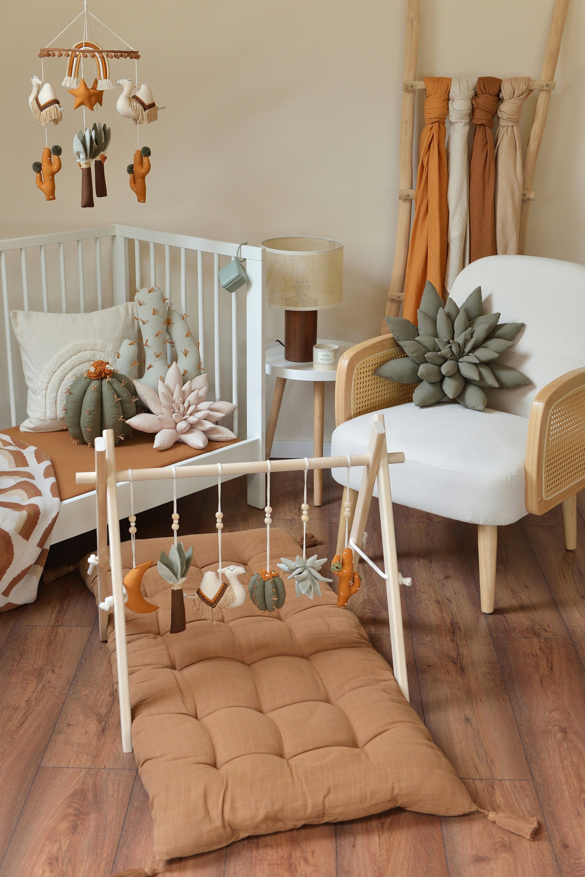 Desert themed baby room with white crib, rattan armchair and baby play gym with hanging toys in the foreground.