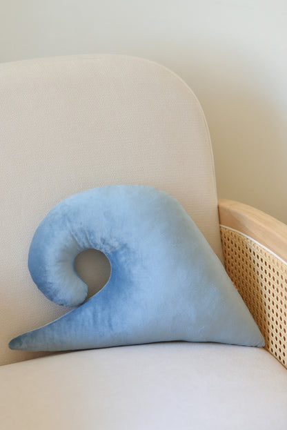 Bakcside of an ocean wave shaped decor pillow placed on a rattan armchair against a white wall.