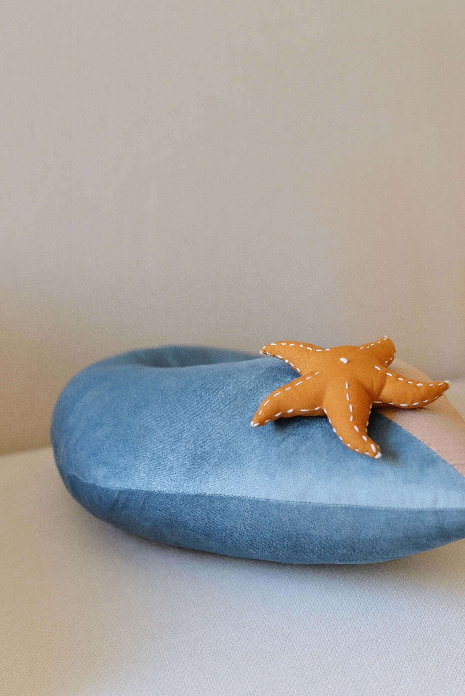 Ocean wave shaped decor pillow from the side with a starfish placed on a rattan armchair.
