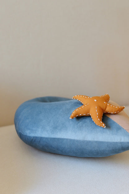 Ocean wave shaped decor pillow from the side with a starfish placed on a rattan armchair.