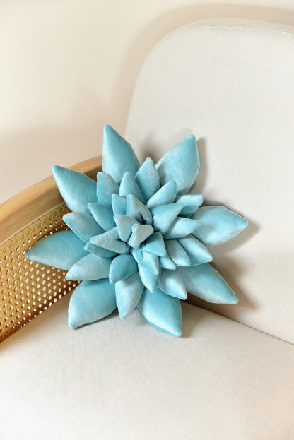 Standard size succulent shaped velvet decor pillow in aqua colour placed on an ivory rattan armchair.
