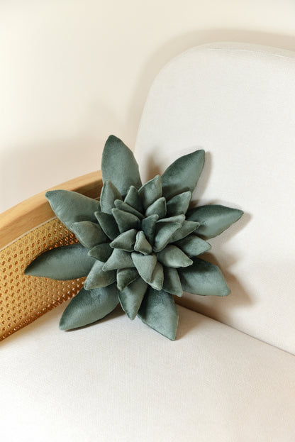 Standard size succulent shaped velvet decor pillow in jade green colour placed on an ivory rattan armchair.