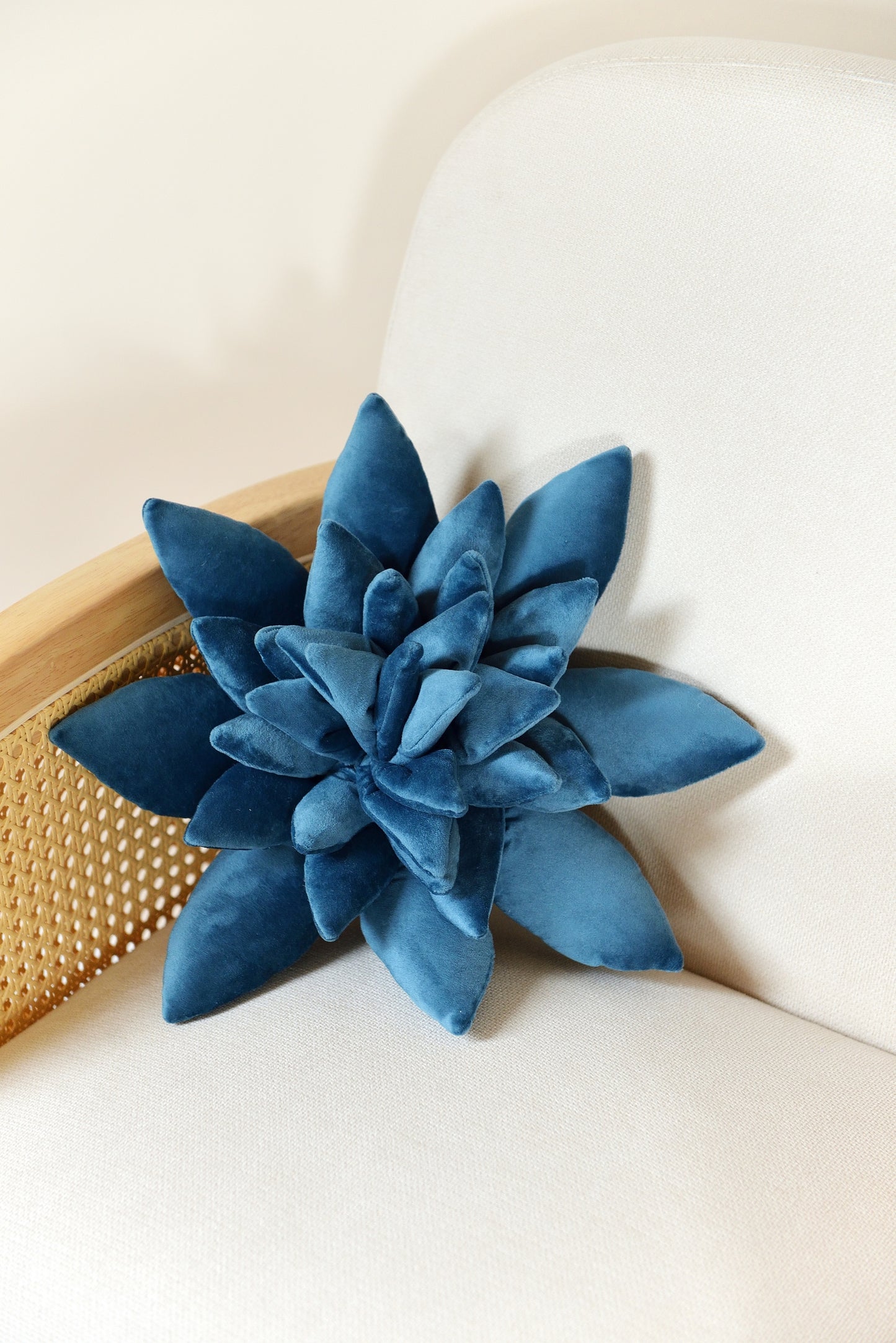 Standard size succulent shaped velvet decor pillow in ocean blue colour placed on an ivory rattan armchair.