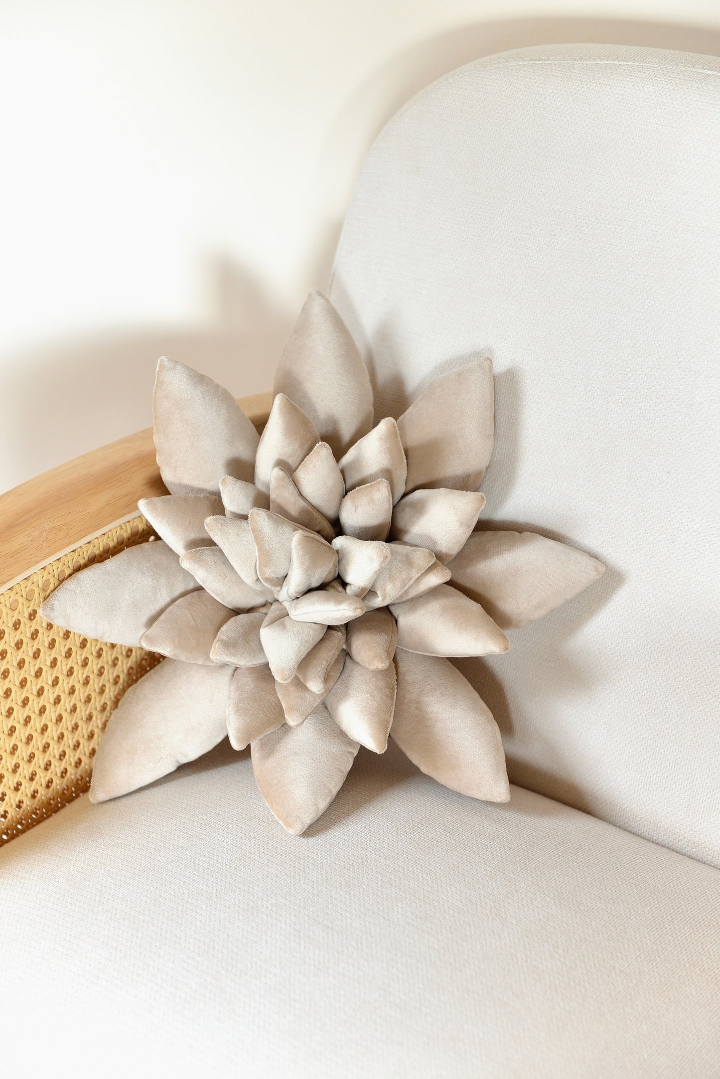 Standard size succulent shaped velvet decor pillow in pearl colour placed on an ivory rattan armchair.