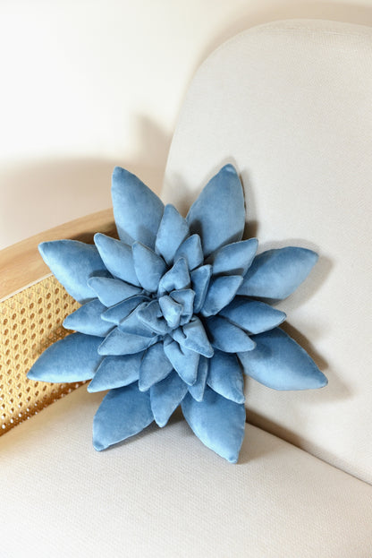 Standard size succulent shaped velvet decor pillow in sky blue colour placed on an ivory rattan armchair.