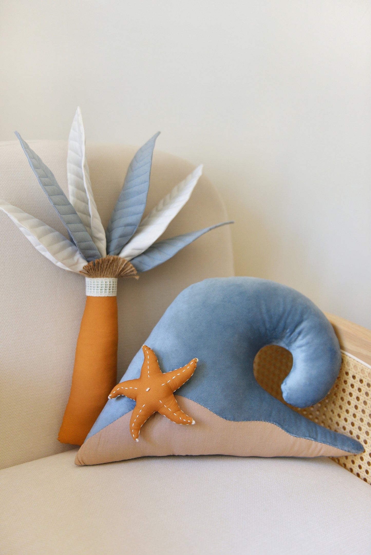 Steal Blue Palm Tree and Wave Decor Pillow Set by Boho Baby Heaven featuring sky blue velvet wave pillow with ochre starfish and palm tree decor pillow placed on an armchair.