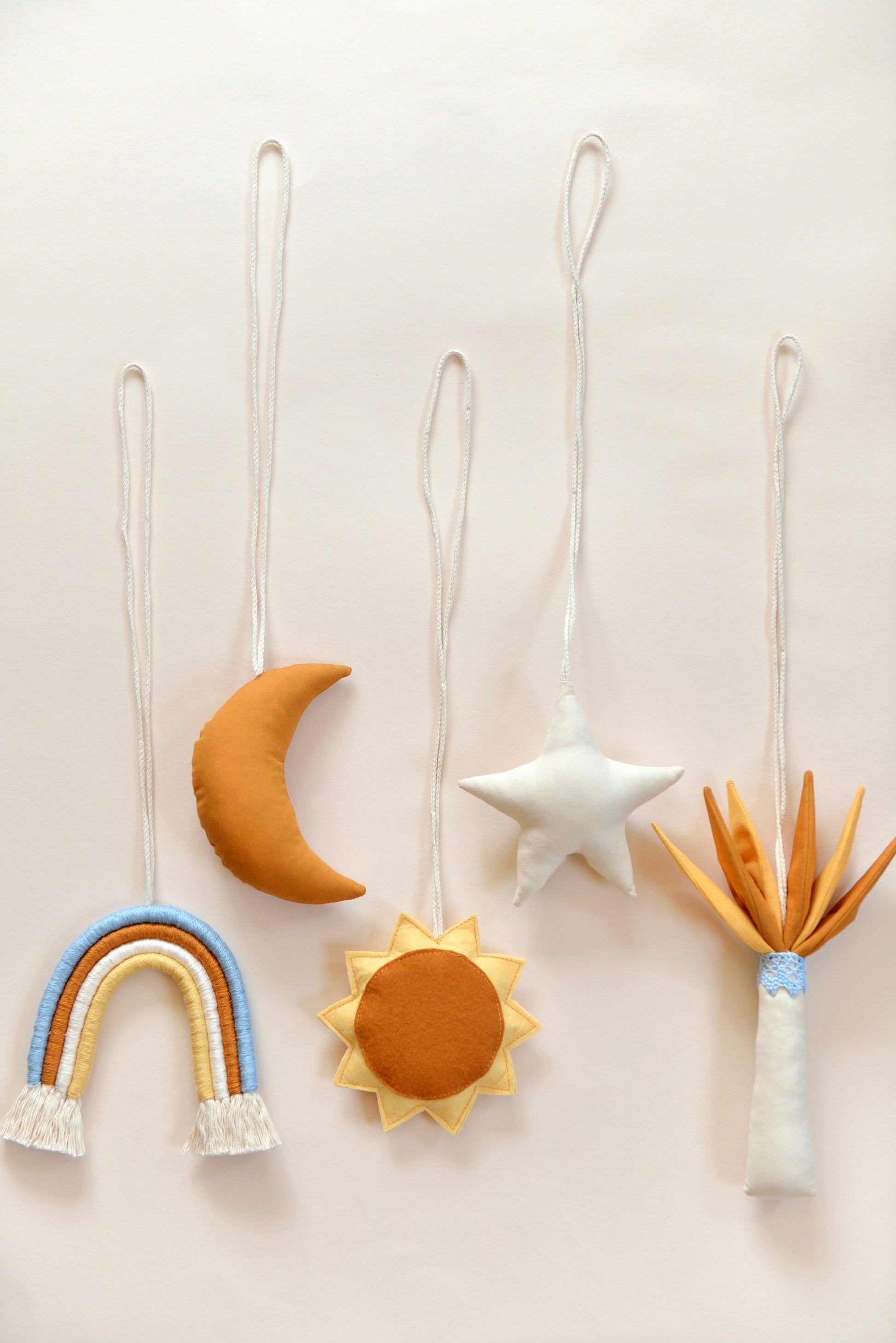 Flatlay of handmade hanging baby play gym toys against a light background: rainbow, moon, sun, star, palm tree.