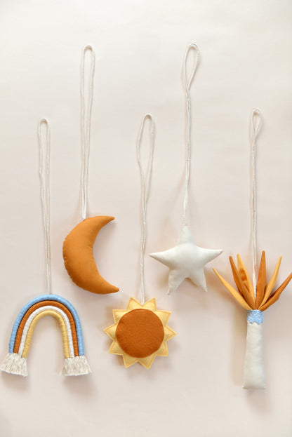 Flatlay of handmade hanging baby play gym toys against a light background: rainbow, moon, sun, star, palm tree.