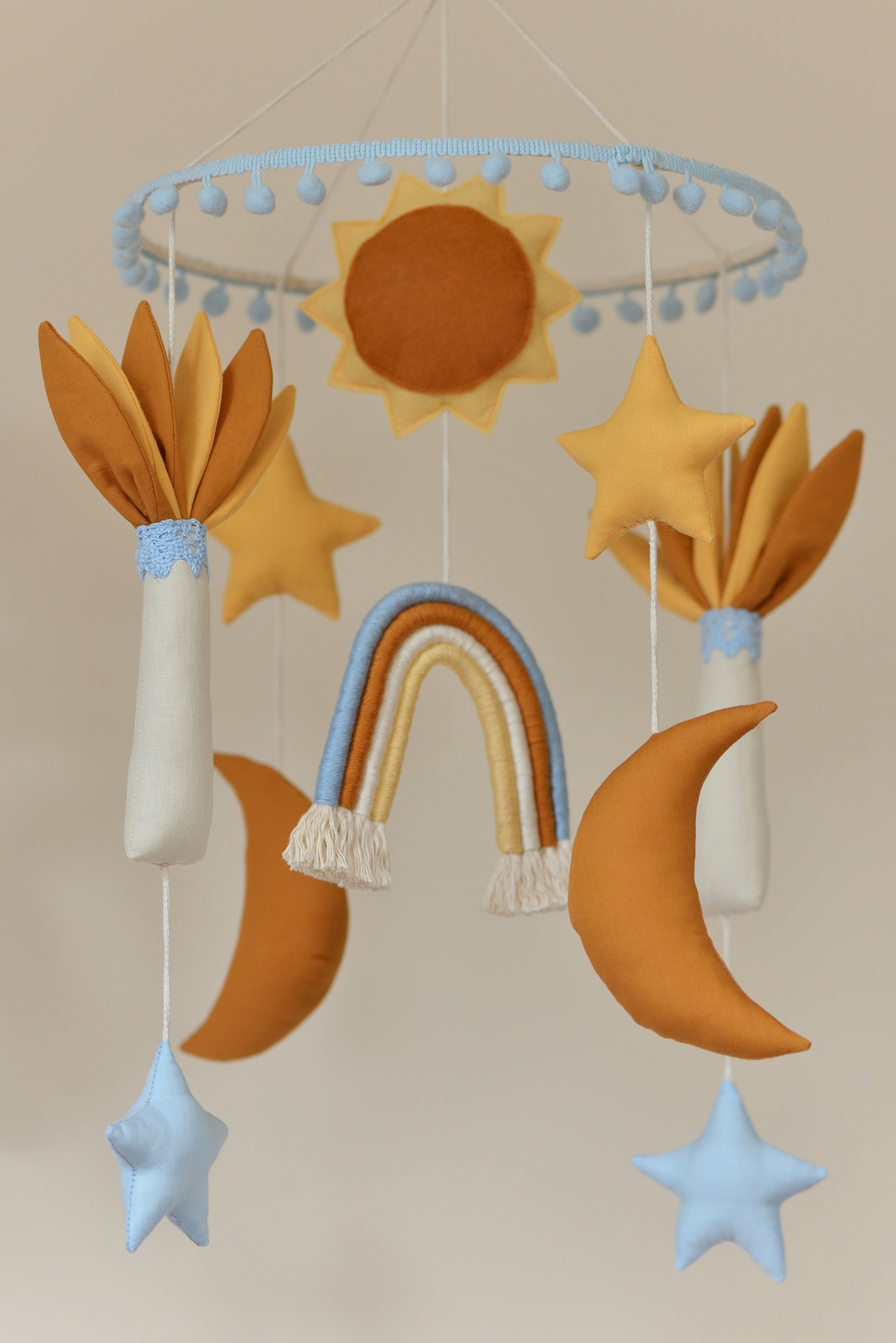 Baby nursery mobile featuring sun, stars, rainbow, and moons and palm trees in ivory, sky blue, yellow and rust shades.