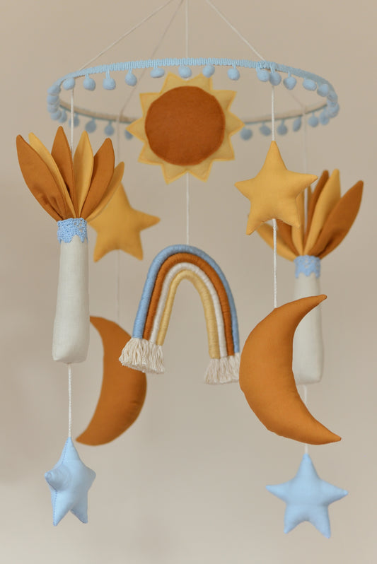 Baby nursery mobile featuring sun, stars, rainbow, and moons and palm trees in ivory, sky blue, yellow and rust shades.