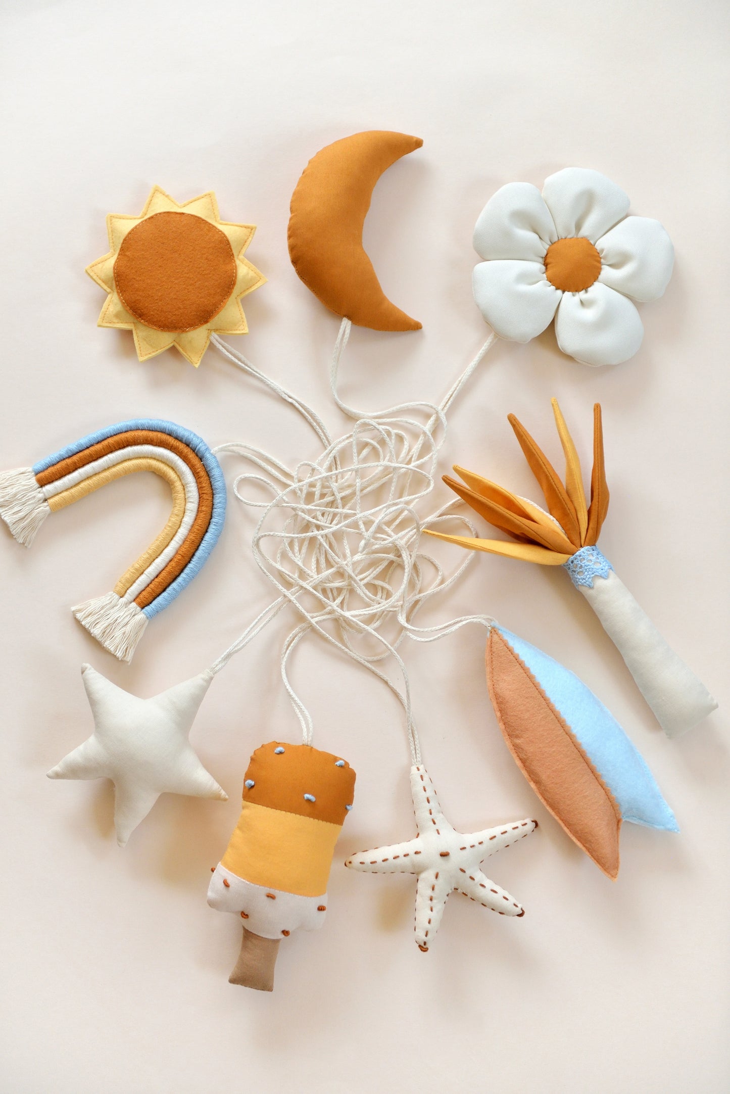 Flatlay of handmade hanging baby play gym toys against a light background: popsickle, starfish, surf board, palm tree, palm tree, daisy, moon, sun, rainbow, star.