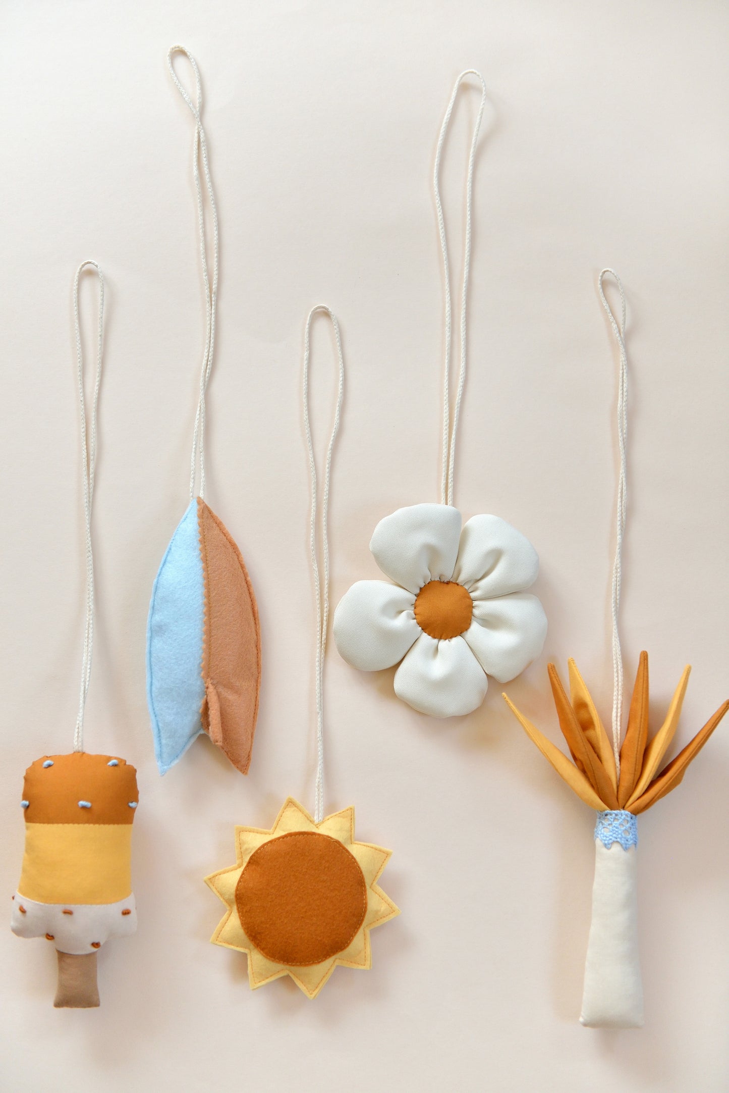 Flatlay of handmade hanging baby play gym toys against a light background: popsickle, surf board, sun, daisy, palm tree.