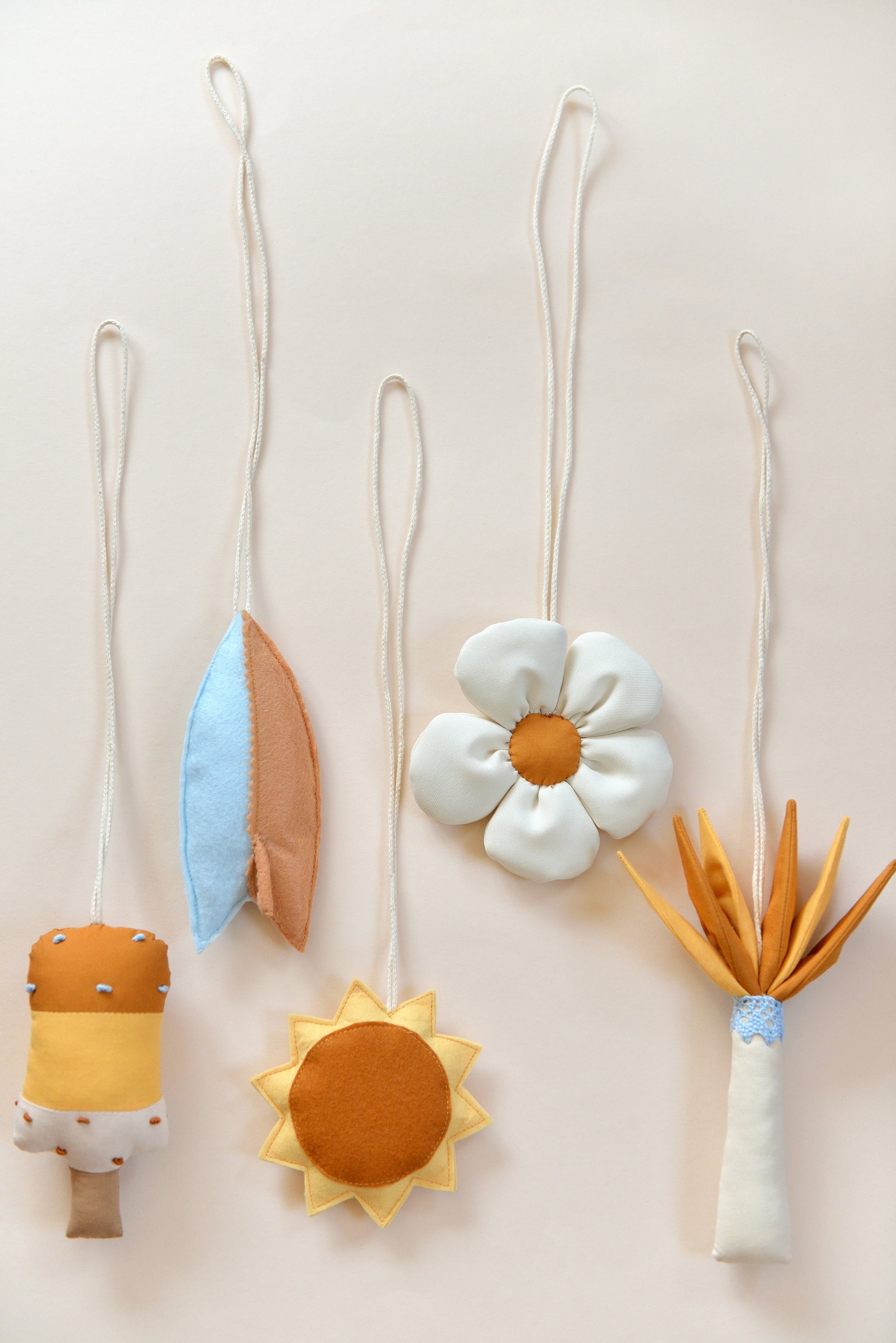 Flatlay of handmade hanging baby play gym toys against a light background: popsickle, surf board, sun, daisy, palm tree.