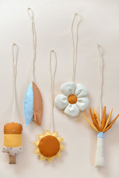 Flatlay of handmade hanging baby play gym toys against a light background: popsickle, surf board, sun, daisy, palm tree.