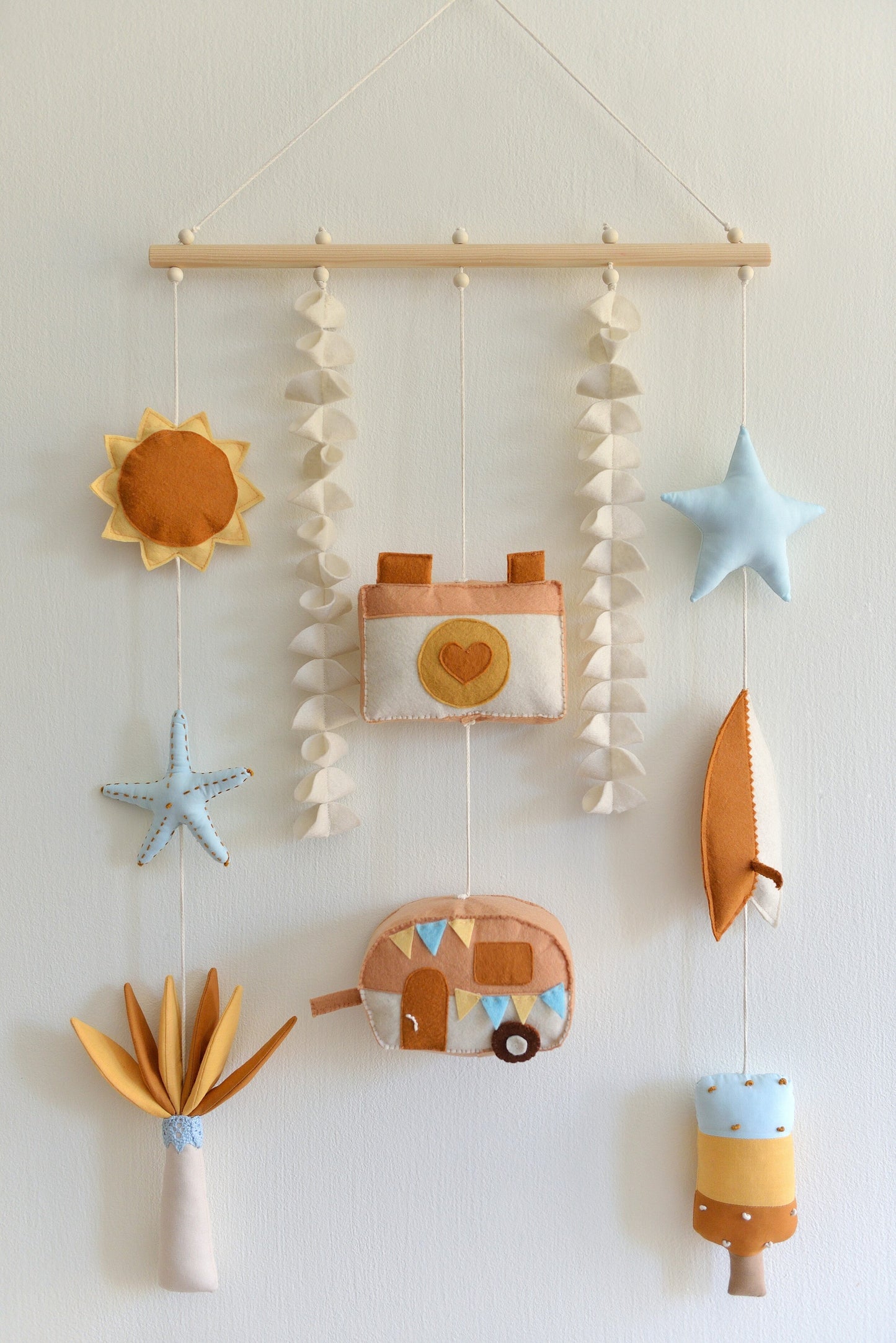 Decorative wall hanging (rod-Hanging Bunting) with colorful felt shapes against a white background. Figures hang off a wooden rod: sun, starfish, palm tree, camera, camper van, star, surf board, popsicle.