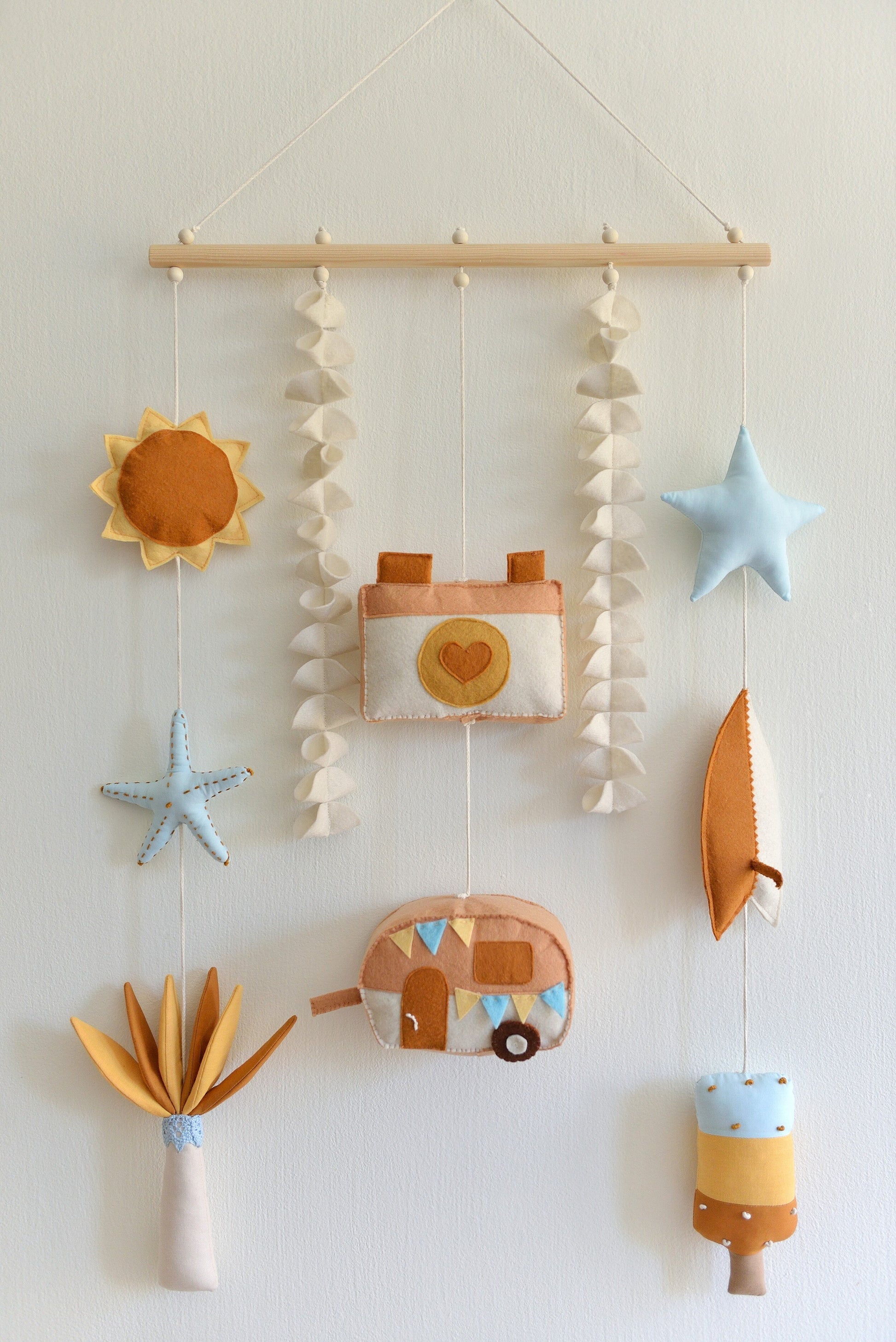Decorative wall hanging (rod-Hanging Bunting) with colorful felt shapes against a white background. Figures hang off a wooden rod: sun, starfish, palm tree, camera, camper van, star, surf board, popsicle.