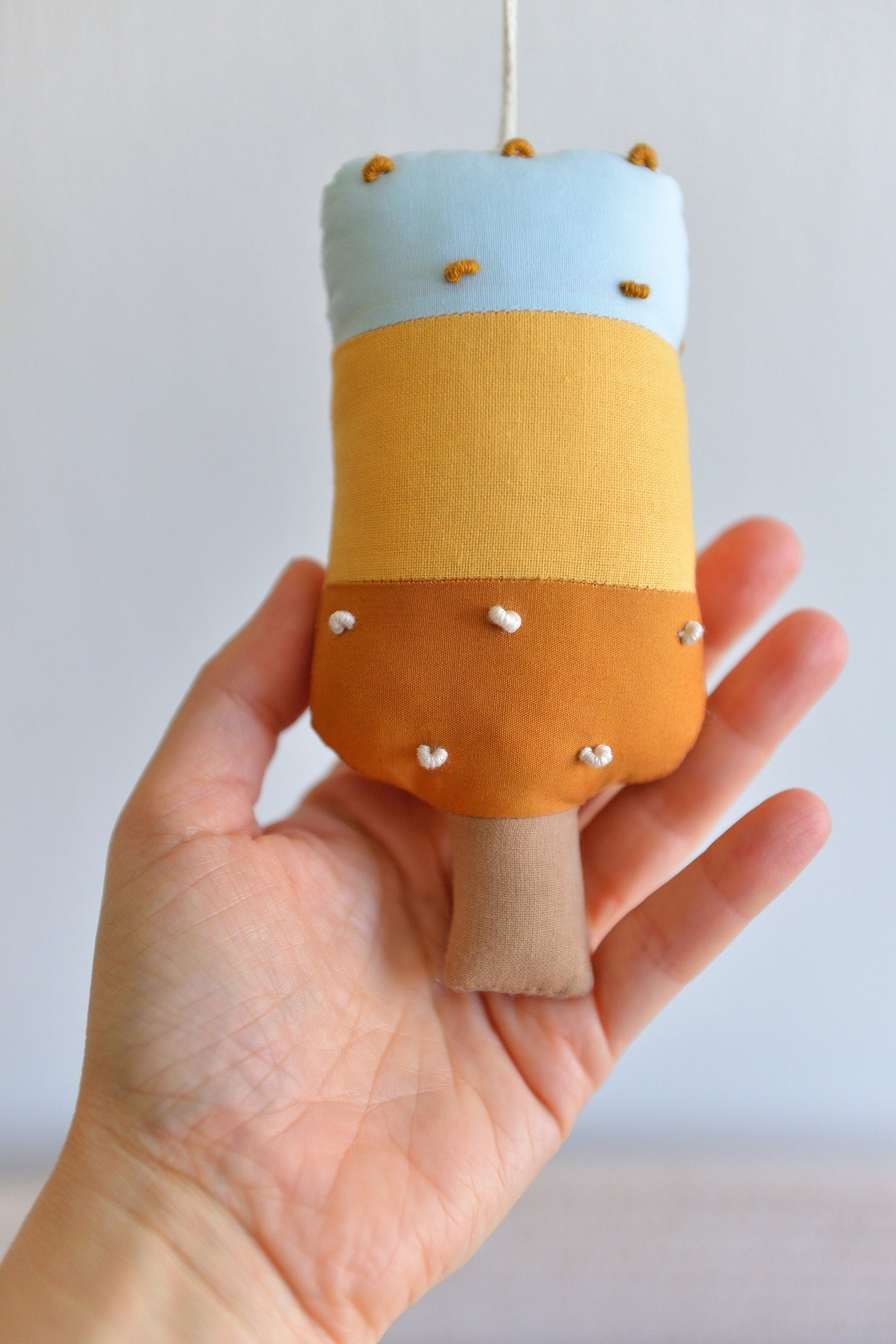 Hand holding a small popsicle figure with a light blue top, amber middle and ochre bottom.