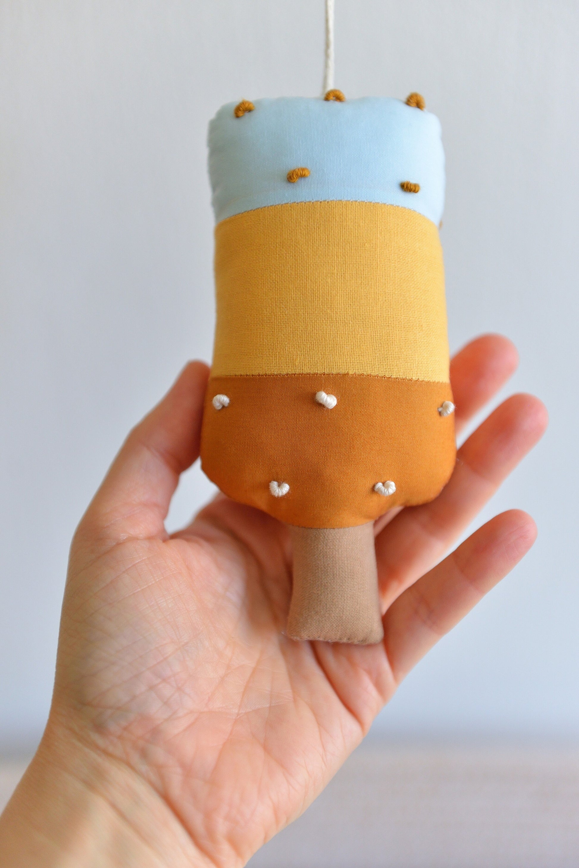 Hand holding a small popsicle figure with a light blue top, amber middle and ochre bottom.