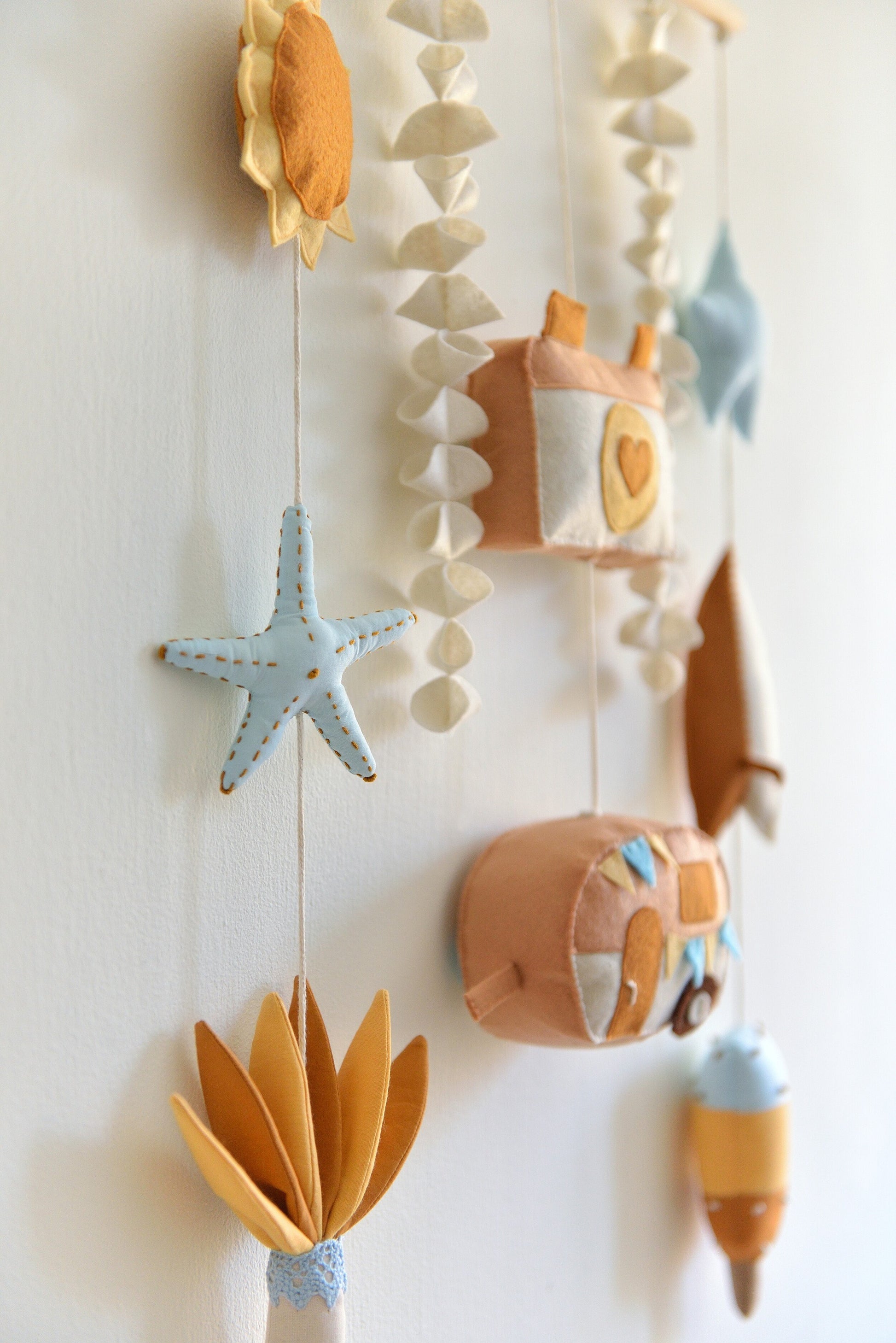 Close up of decorative wall hanging (rod-hanging bunting) with colorful felt shapes against a white background. Figures hang off a wooden rod: sun, starfish, palm tree, camera, camper van, star, surf board, popsicle.