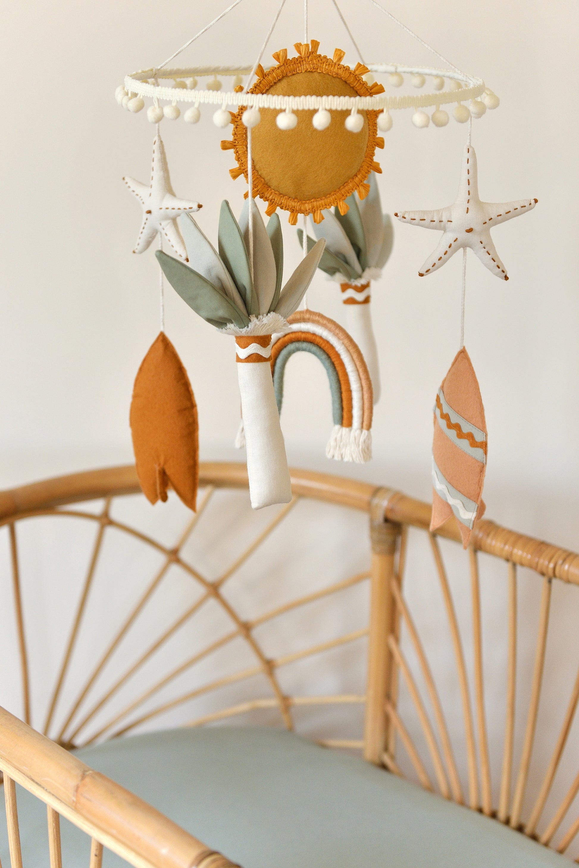 Surf baby mobile hung over a rattan bassinet. Figures include sun, starfish, surf boards, palms. 
