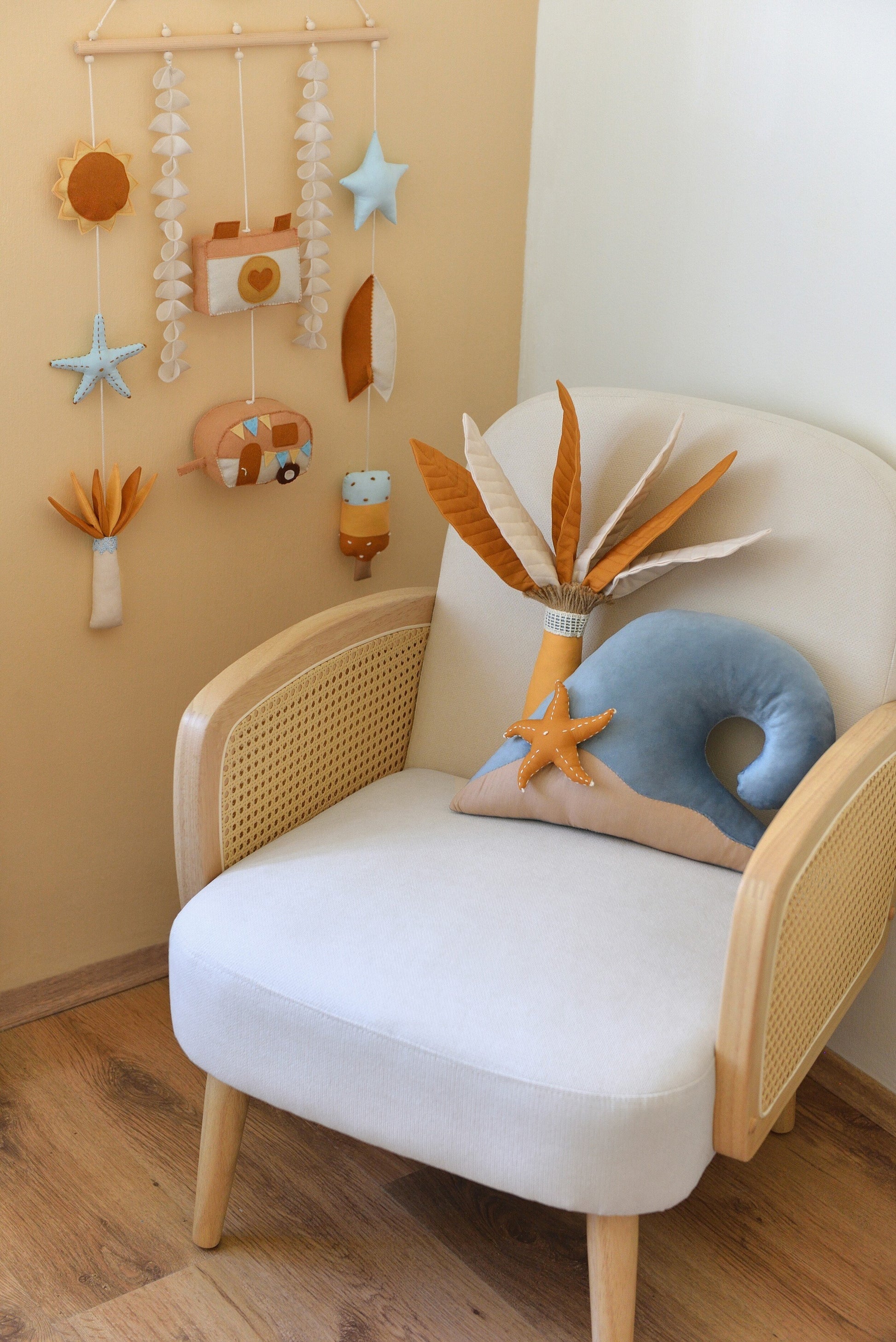 Ivory rattan armchair with palm tree and ocean wave shaped pillows and a surf-themed rod-hanging bunting in a baby room.