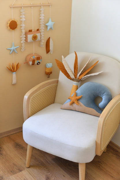 Ivory rattan armchair with palm tree and ocean wave shaped pillows and a surf-themed rod-hanging bunting in a baby room.