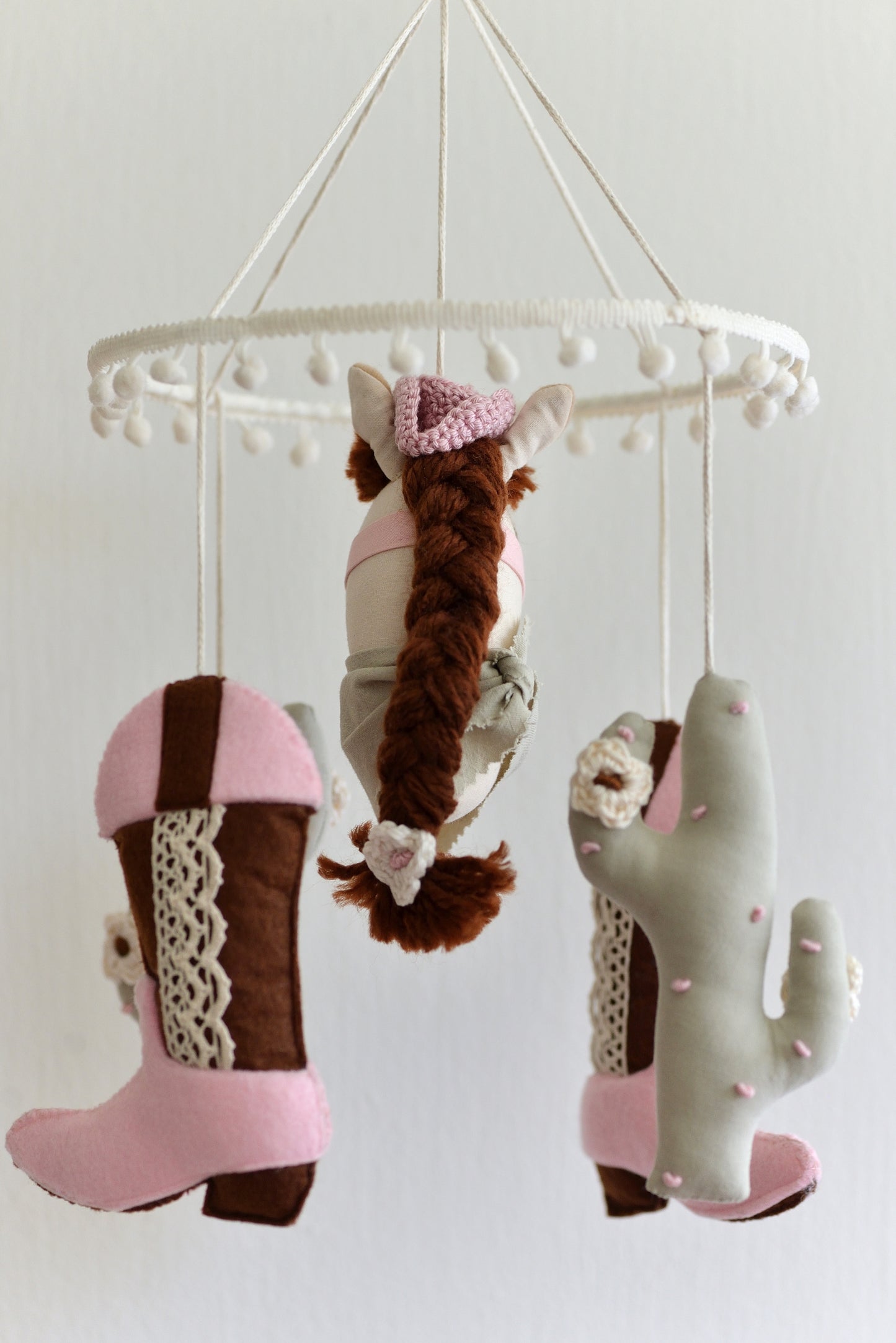 Cowgirl themed baby mobile with horse, cacti and cowgirl boots hanging against a white background.