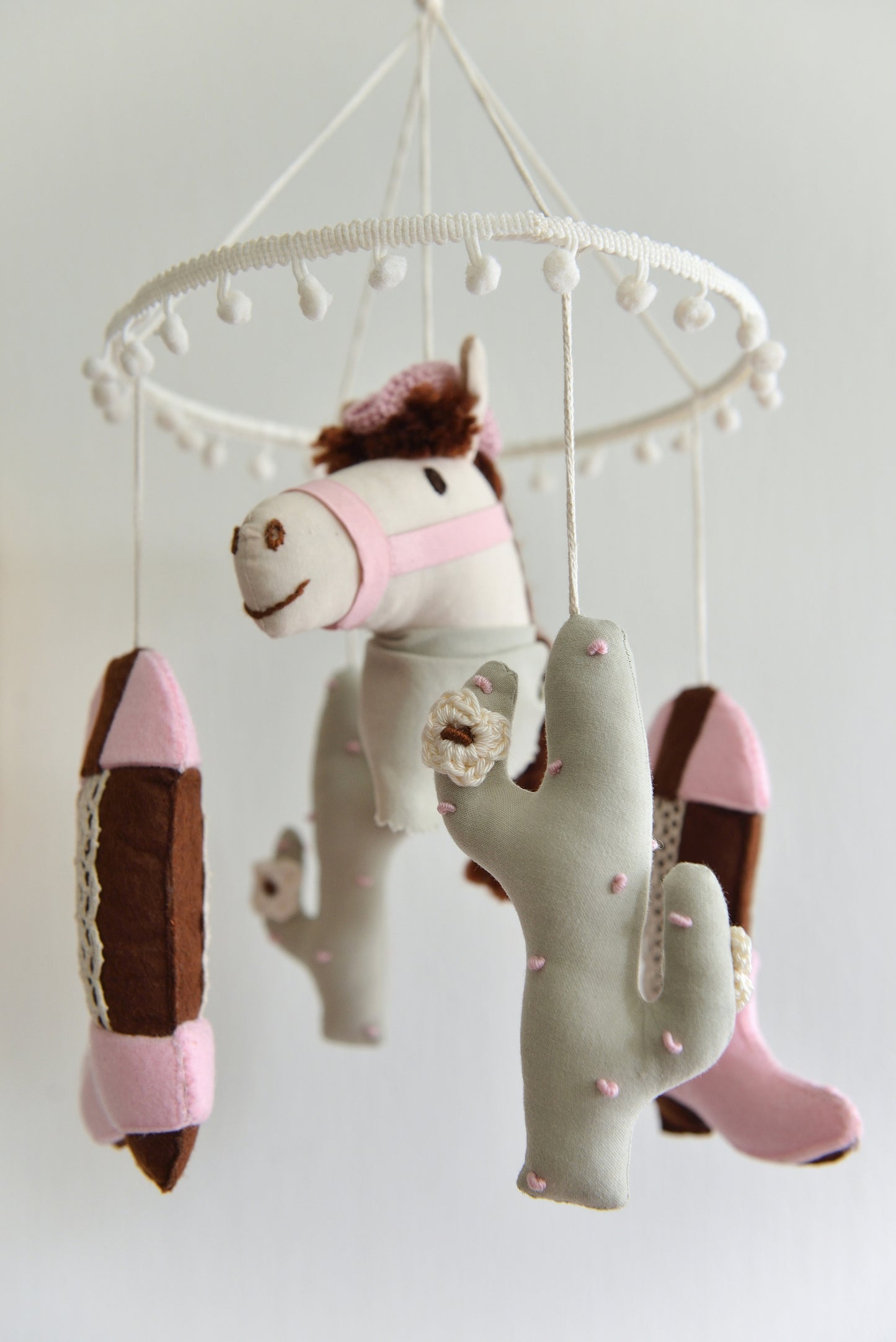 Cowgirl themed baby mobile with horse, cacti and cowgirl boots hanging against a white background.