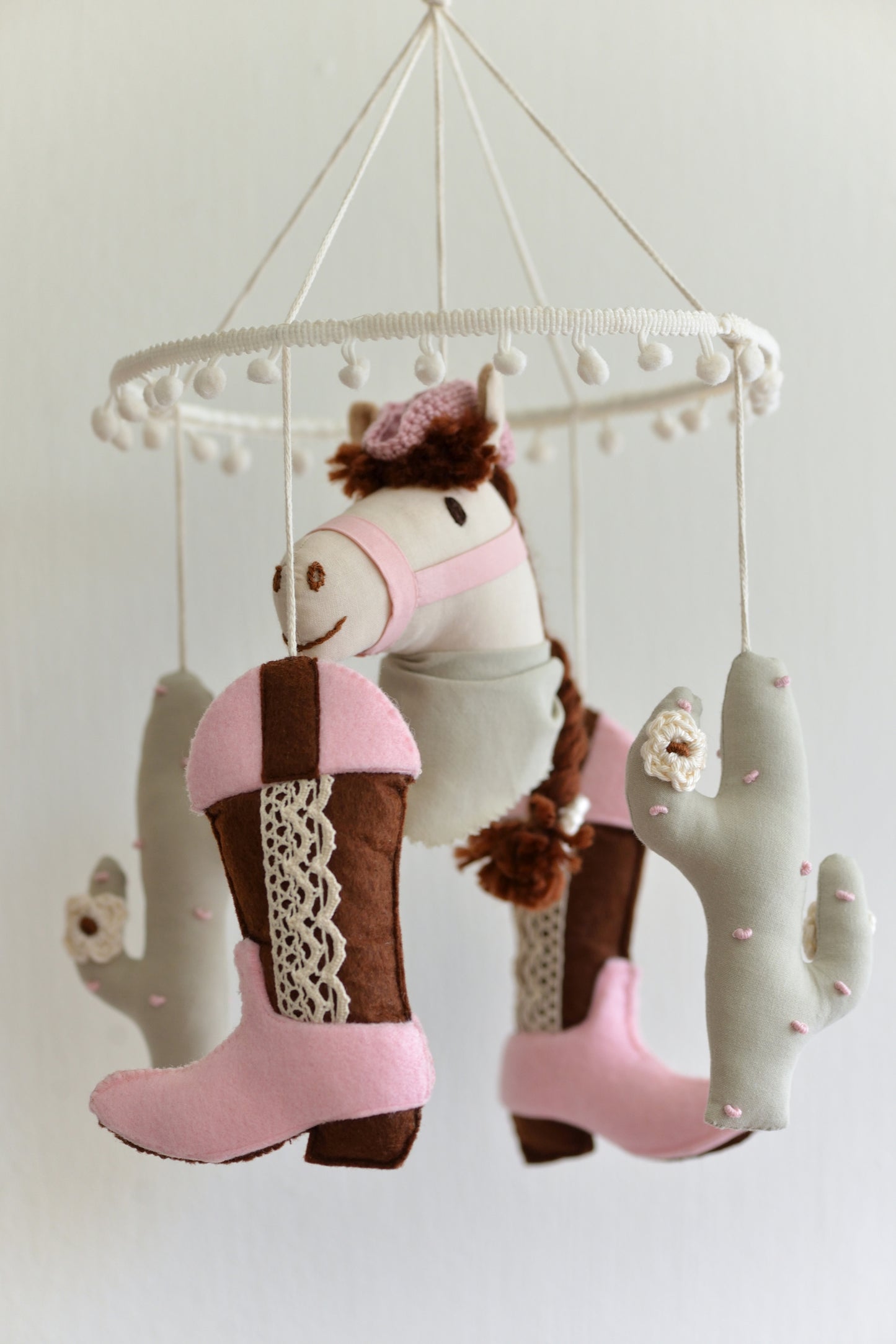 Cowgirl themed baby mobile with horse, cacti and cowgirl boots hanging against a white background.