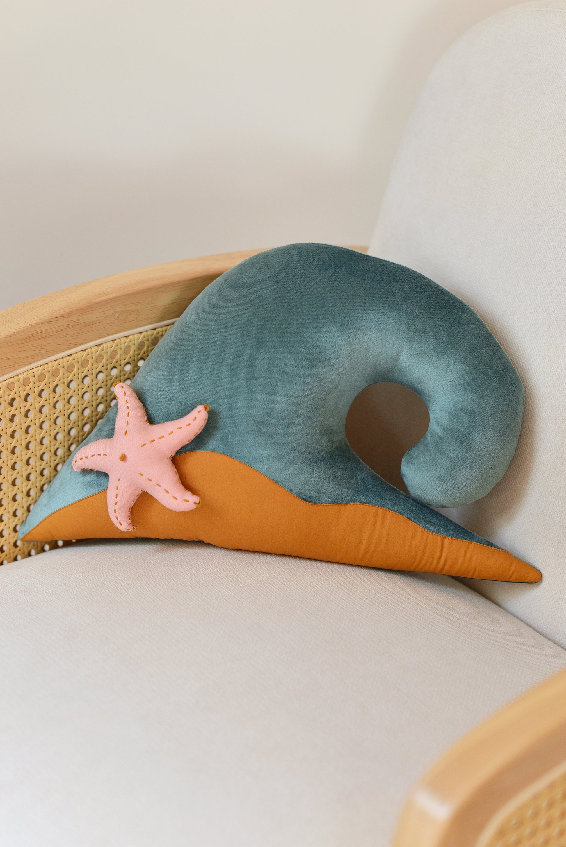 Ocean Blue wave shaped decor pillow with dark mint green sandy base and coral red starfish on an ivory rattan armchair.